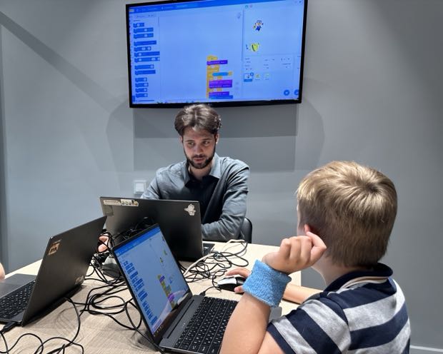 Занятие в филиале: на большом экране проект в Scratch, ребёнок повторяет его у себя на ноутбуке